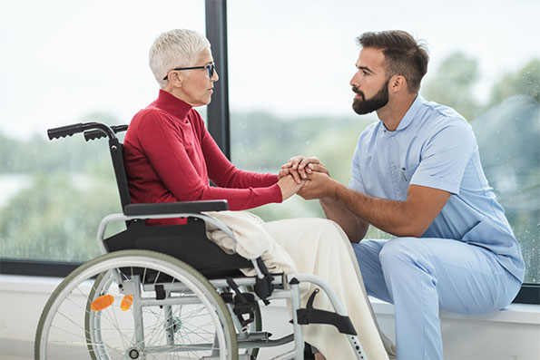 Male worker with elderly woman in wheelchair in nursing home that is protected with professional liability insurance coverage.