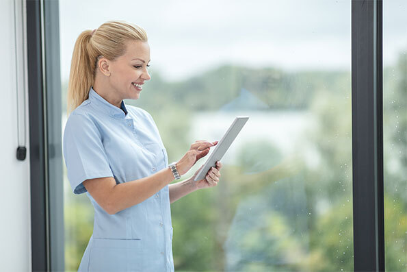 Woman worker smiling while holding tablet getting quote from residential care facility workers compensation insurance broker.
